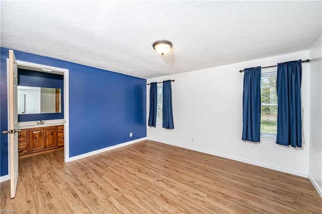 unfurnished room with a textured ceiling, a sink, light wood-style flooring, and baseboards