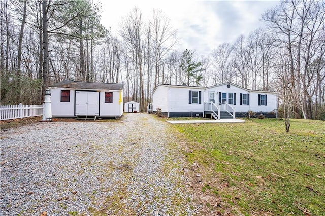 manufactured / mobile home with an outdoor structure, fence, driveway, a shed, and a front yard