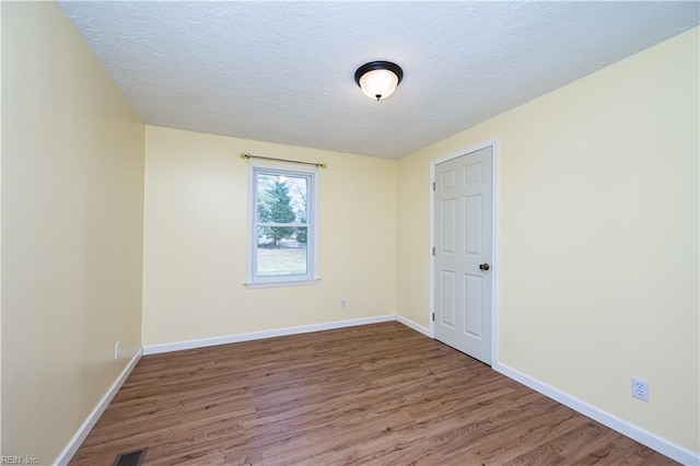 empty room featuring a textured ceiling, wood finished floors, visible vents, and baseboards