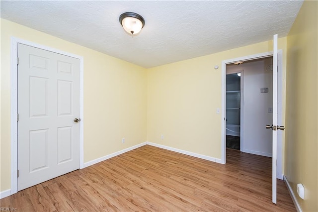 empty room with light wood-style flooring, baseboards, and a textured ceiling