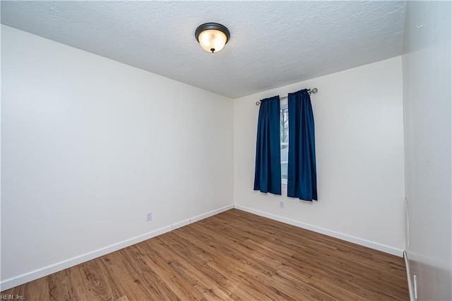 unfurnished room featuring a textured ceiling, wood finished floors, and baseboards