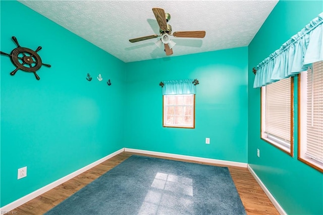 empty room with ceiling fan, a textured ceiling, baseboards, and wood finished floors