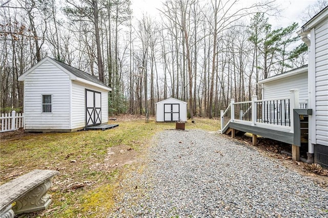 view of yard featuring a storage shed, an outdoor structure, fence, a wooden deck, and gravel driveway