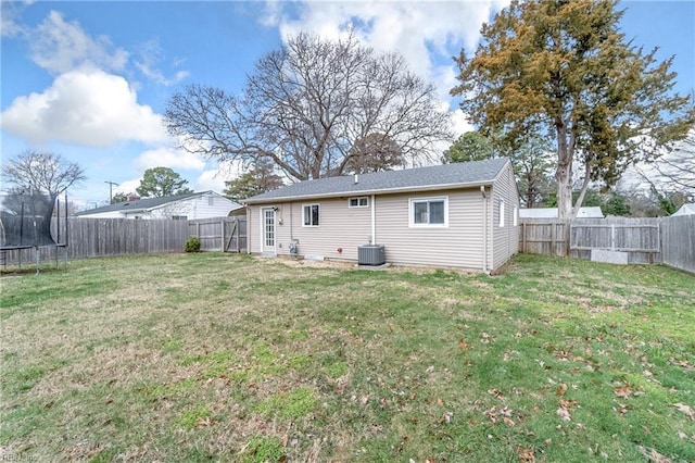 rear view of property featuring a yard, a trampoline, a fenced backyard, and central air condition unit