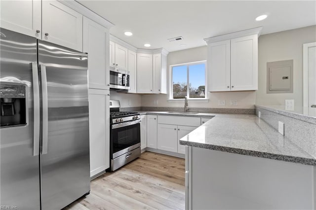 kitchen with a peninsula, appliances with stainless steel finishes, light wood-type flooring, and white cabinets