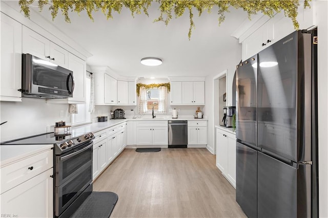 kitchen with light countertops, light wood-style flooring, appliances with stainless steel finishes, white cabinetry, and a sink