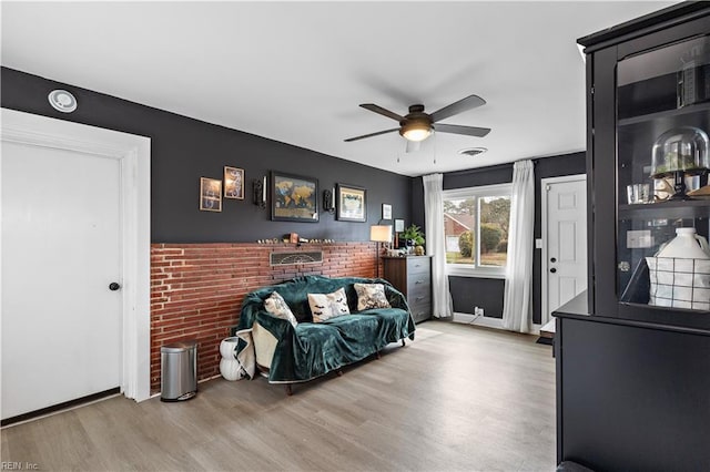 living area featuring visible vents, baseboards, a ceiling fan, brick wall, and wood finished floors