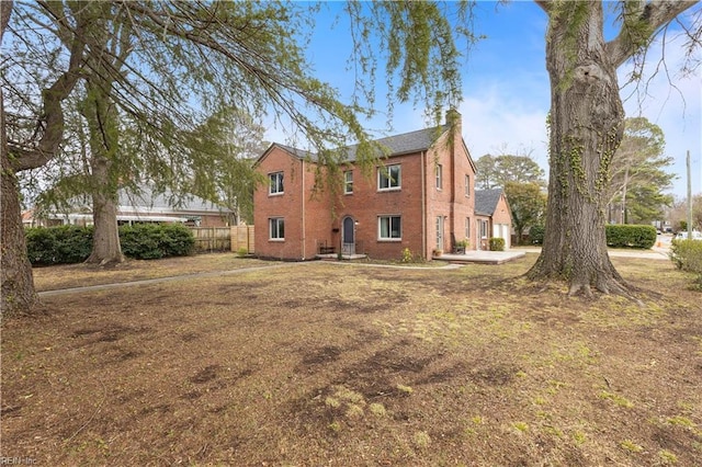 rear view of property featuring brick siding, a chimney, and fence