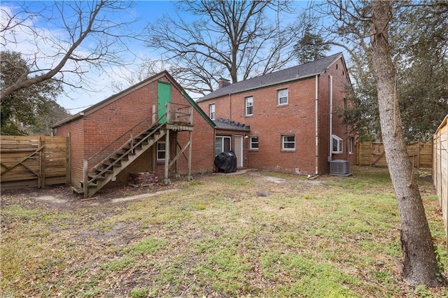 back of house featuring central AC unit, a fenced backyard, stairway, a yard, and brick siding