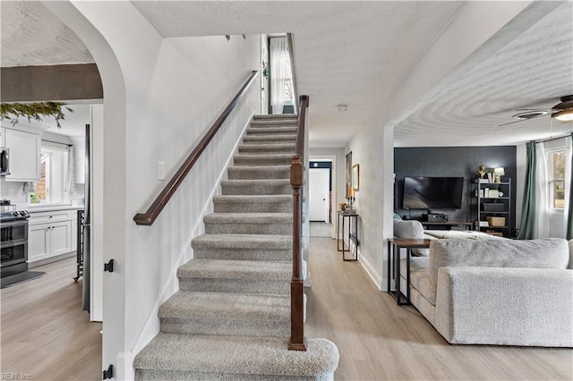 staircase with a ceiling fan, arched walkways, baseboards, and wood finished floors