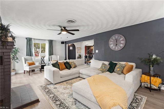 living area with arched walkways, an accent wall, wood finished floors, visible vents, and a ceiling fan