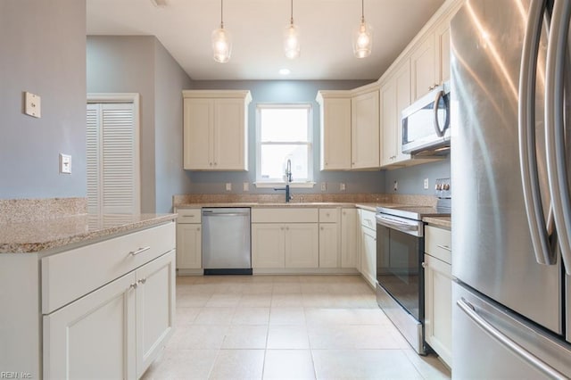 kitchen featuring light stone countertops, pendant lighting, stainless steel appliances, and a sink