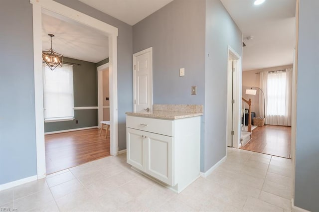 kitchen featuring light stone counters, a notable chandelier, light tile patterned floors, white cabinetry, and baseboards