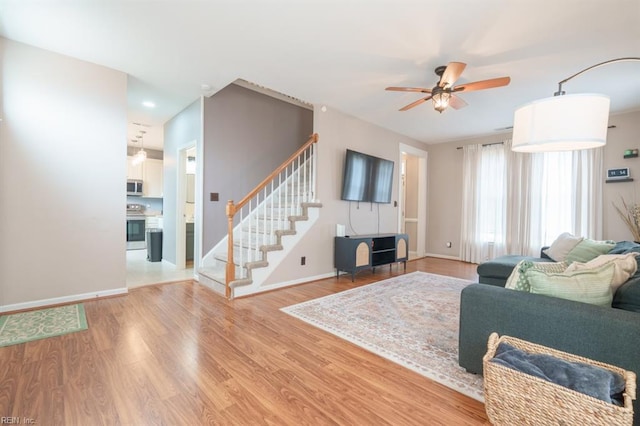 living room with light wood-style flooring, ceiling fan, stairway, and baseboards