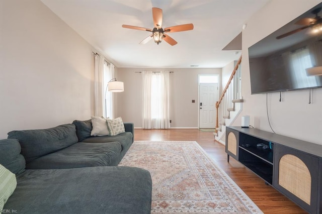 living area with stairs, ceiling fan, baseboards, and wood finished floors