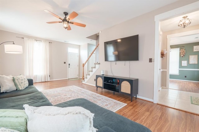 living room with a ceiling fan, wood finished floors, baseboards, and stairs