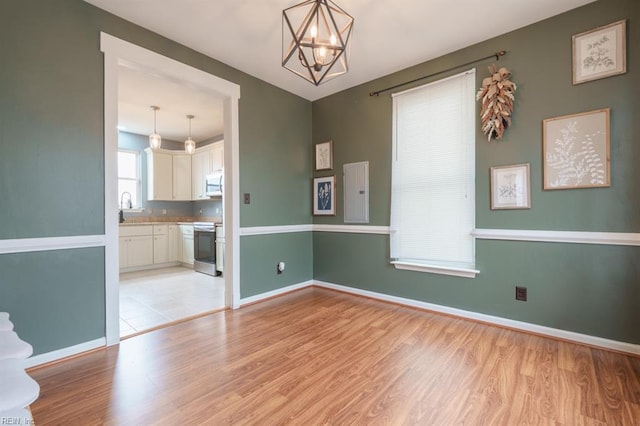 empty room featuring light wood-type flooring, an inviting chandelier, and baseboards