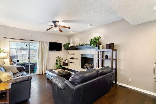 living room featuring a textured ceiling, a tiled fireplace, visible vents, and wood finished floors