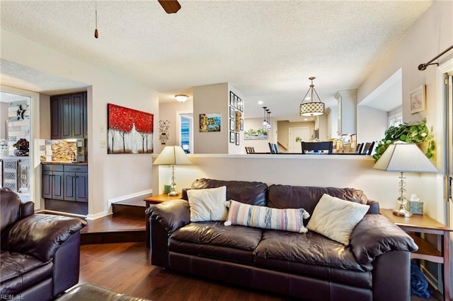 living area featuring a textured ceiling, wood finished floors, a ceiling fan, and baseboards