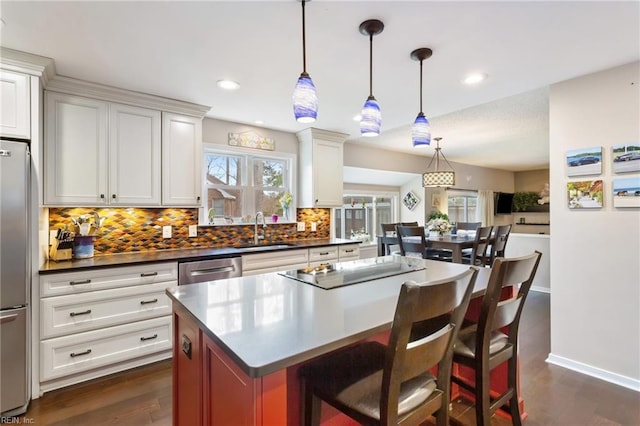 kitchen with a center island, stainless steel appliances, dark countertops, backsplash, and a sink