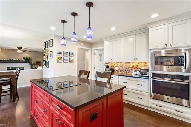 kitchen with dark wood-style flooring, dark countertops, backsplash, appliances with stainless steel finishes, and a ceiling fan