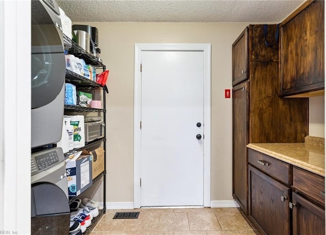 laundry room featuring stacked washer and dryer, a textured ceiling, baseboards, and cabinet space