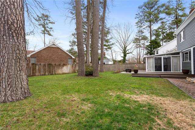 view of yard featuring a deck, a fenced backyard, and a sunroom