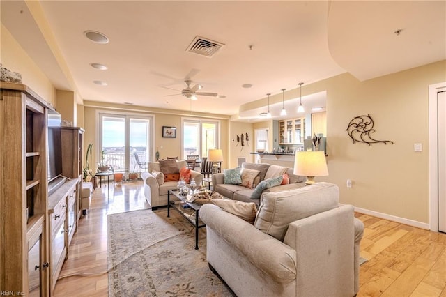 living room featuring baseboards, ceiling fan, visible vents, and light wood-style floors