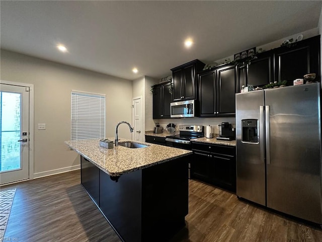 kitchen with dark cabinets, stainless steel appliances, dark wood-type flooring, a sink, and a center island with sink