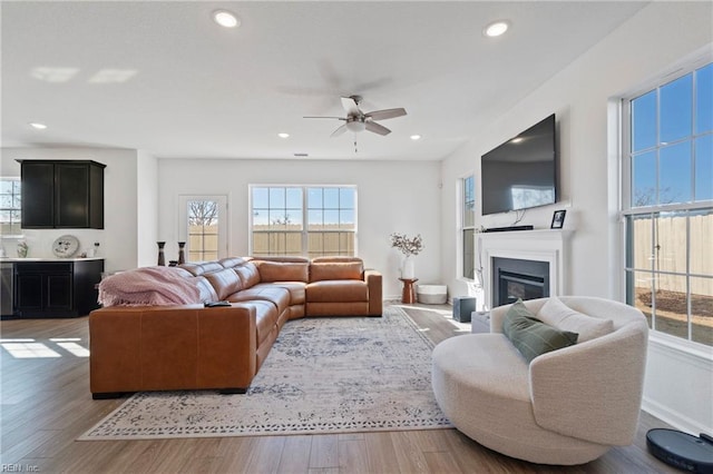 living area featuring ceiling fan, a glass covered fireplace, wood finished floors, and recessed lighting