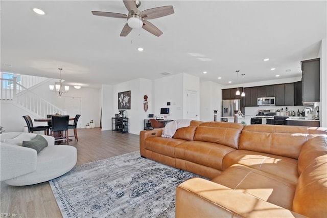 living room with light wood-style flooring, stairs, ceiling fan with notable chandelier, and recessed lighting