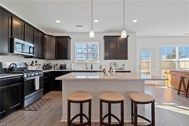 kitchen featuring stainless steel appliances, light stone counters, light wood-type flooring, and a kitchen bar