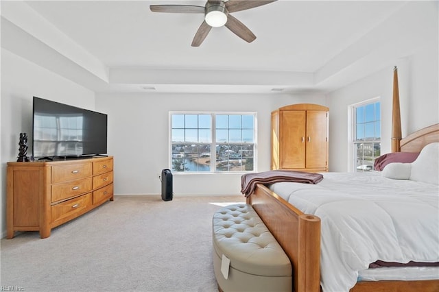 bedroom with a tray ceiling, light carpet, ceiling fan, and baseboards