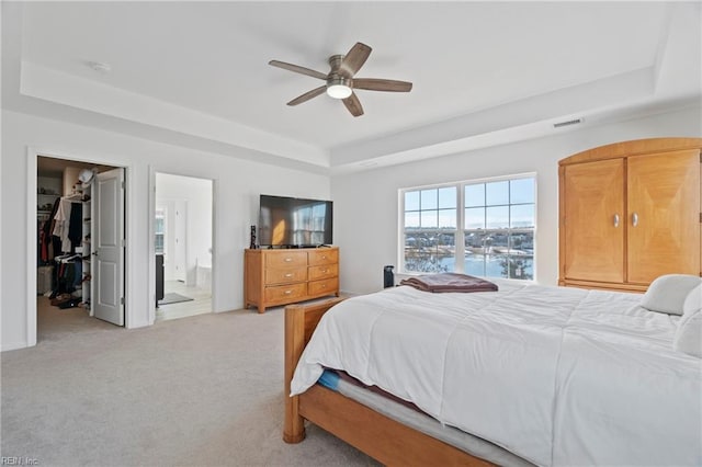 bedroom with a raised ceiling, visible vents, light colored carpet, a spacious closet, and ensuite bathroom