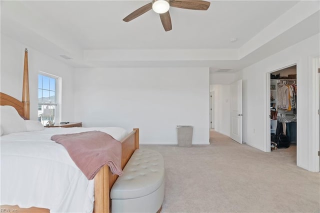 bedroom featuring light carpet, a raised ceiling, a walk in closet, and a ceiling fan