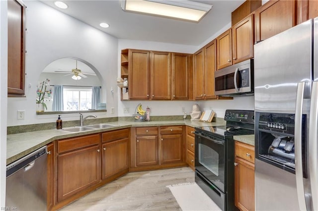 kitchen featuring arched walkways, light wood-style flooring, a sink, appliances with stainless steel finishes, and brown cabinets