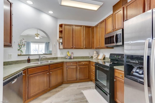 kitchen with arched walkways, brown cabinetry, ceiling fan, appliances with stainless steel finishes, and a sink