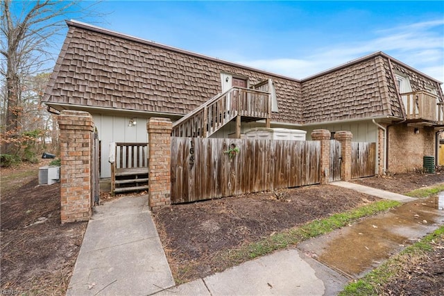 view of front of property with brick siding, mansard roof, board and batten siding, central AC, and fence