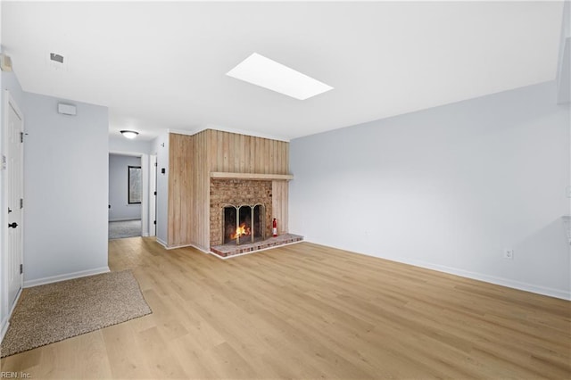 unfurnished living room featuring a skylight, a fireplace, light wood-style flooring, and baseboards