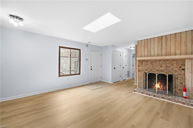 unfurnished living room with light wood-type flooring, a skylight, a brick fireplace, and baseboards