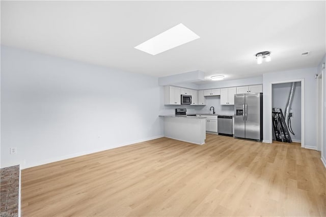 kitchen featuring a skylight, appliances with stainless steel finishes, light countertops, white cabinetry, and a sink