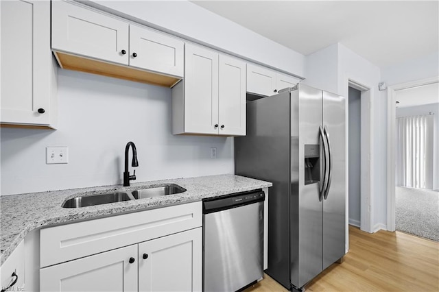 kitchen featuring white cabinets, light wood-style flooring, appliances with stainless steel finishes, light stone countertops, and a sink