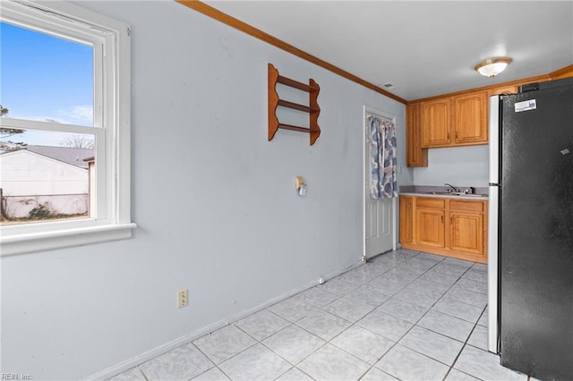 kitchen featuring brown cabinets, crown molding, light countertops, freestanding refrigerator, and light tile patterned flooring