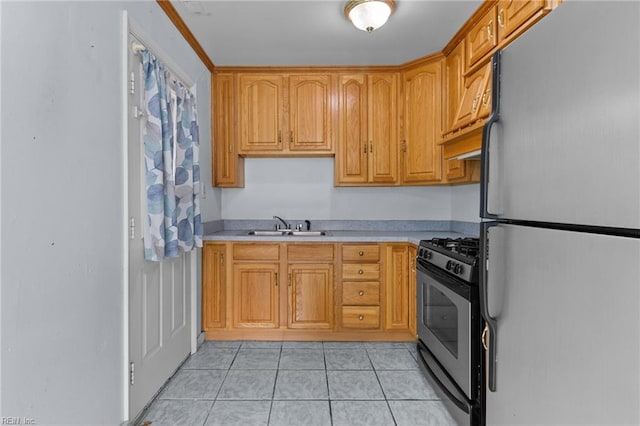 kitchen with light countertops, freestanding refrigerator, light tile patterned flooring, a sink, and stainless steel gas range