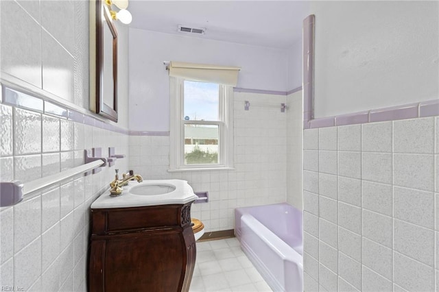 bathroom featuring a wainscoted wall, tile walls, visible vents, a bathing tub, and vanity