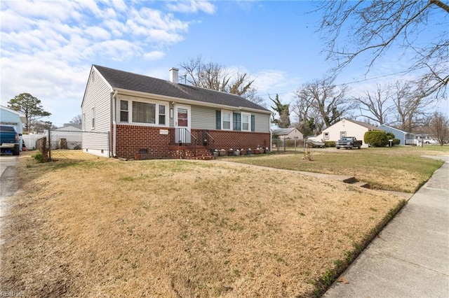 view of front facade with brick siding, a chimney, a front yard, crawl space, and fence