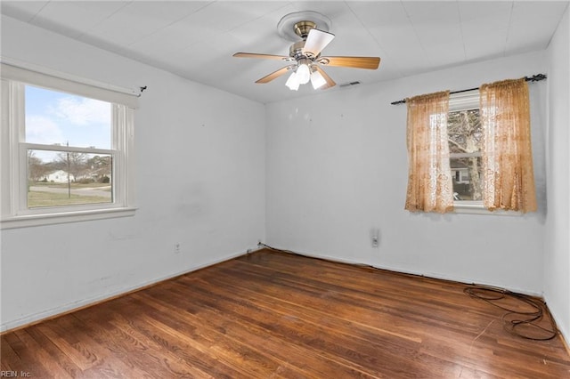 empty room with a wealth of natural light, visible vents, ceiling fan, and wood finished floors