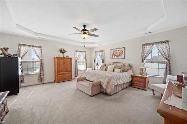 bedroom with a tray ceiling, light colored carpet, visible vents, and a textured ceiling