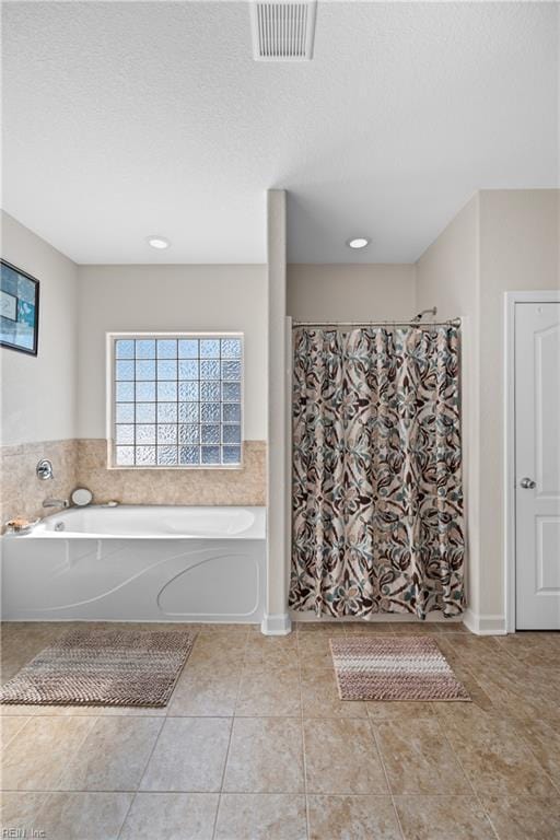 bathroom featuring a textured ceiling, tile patterned flooring, a garden tub, and visible vents