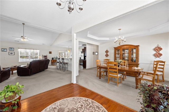 carpeted dining room with wood finished floors, a raised ceiling, baseboards, and ceiling fan with notable chandelier